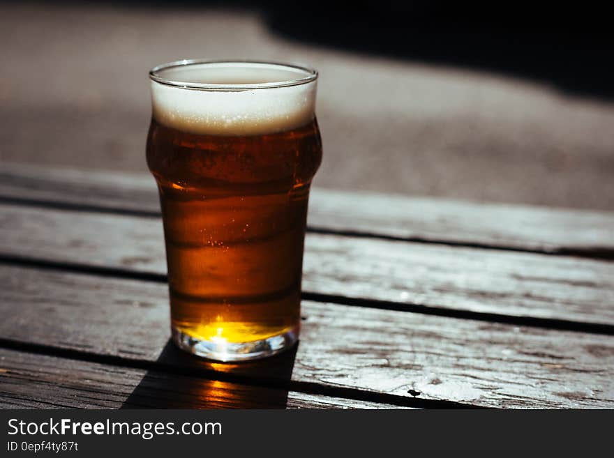 Close up of glass of amber ale on wooden tabletop outdoors. Close up of glass of amber ale on wooden tabletop outdoors.