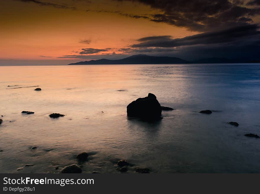 Rocks along coastline against blue and orange skies at sunset. Rocks along coastline against blue and orange skies at sunset.