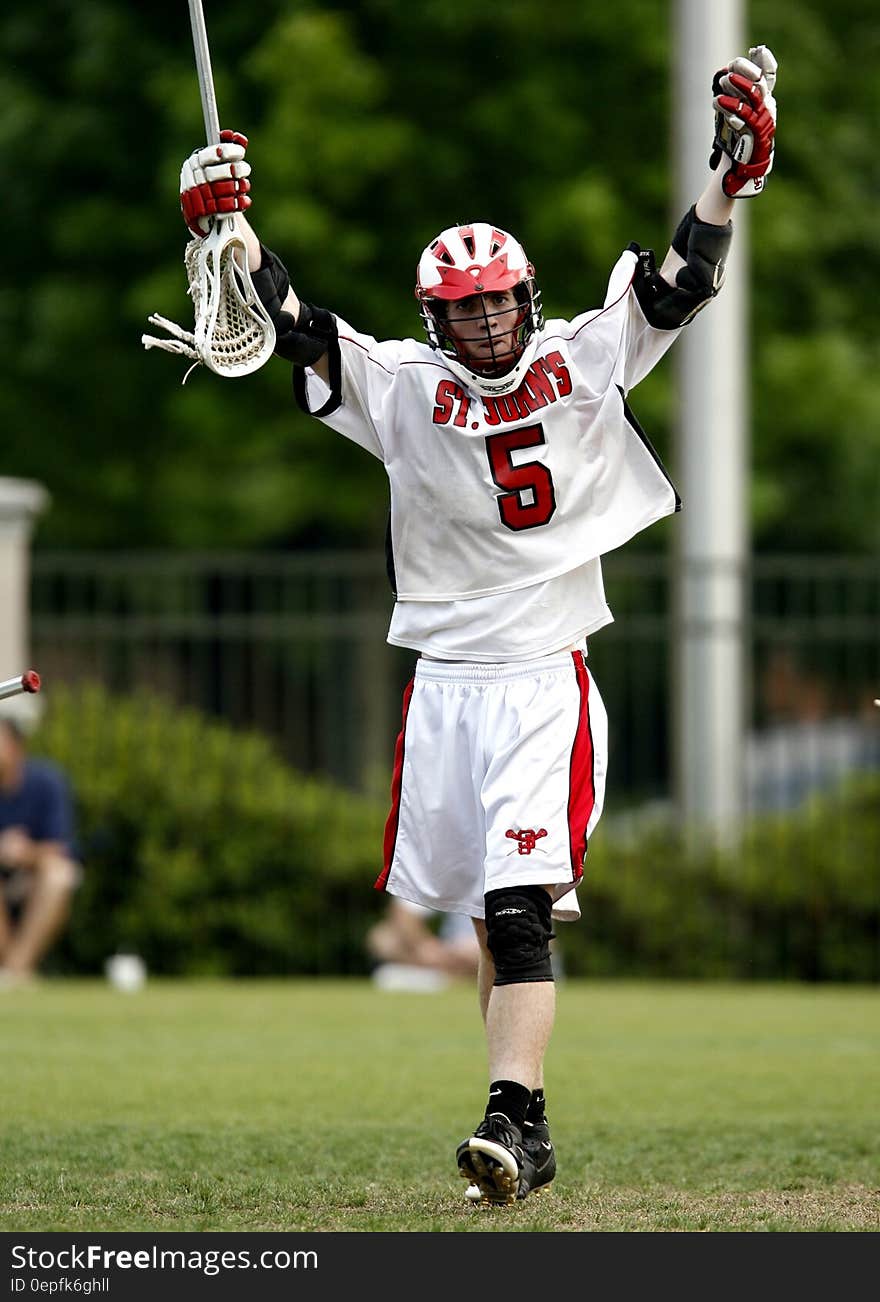 Man Holding White Lacrosse Stick Standing on Green Grass Field during Daytime