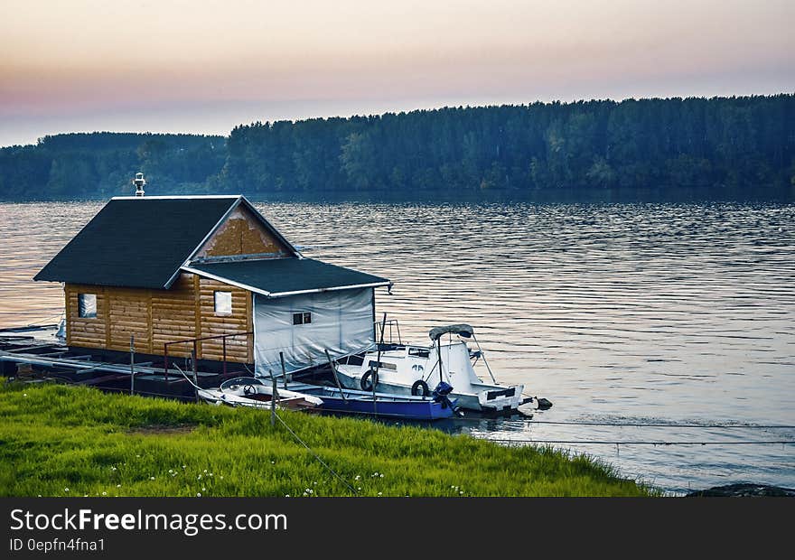 White Boat Beside Wooden House on Water Near Forest