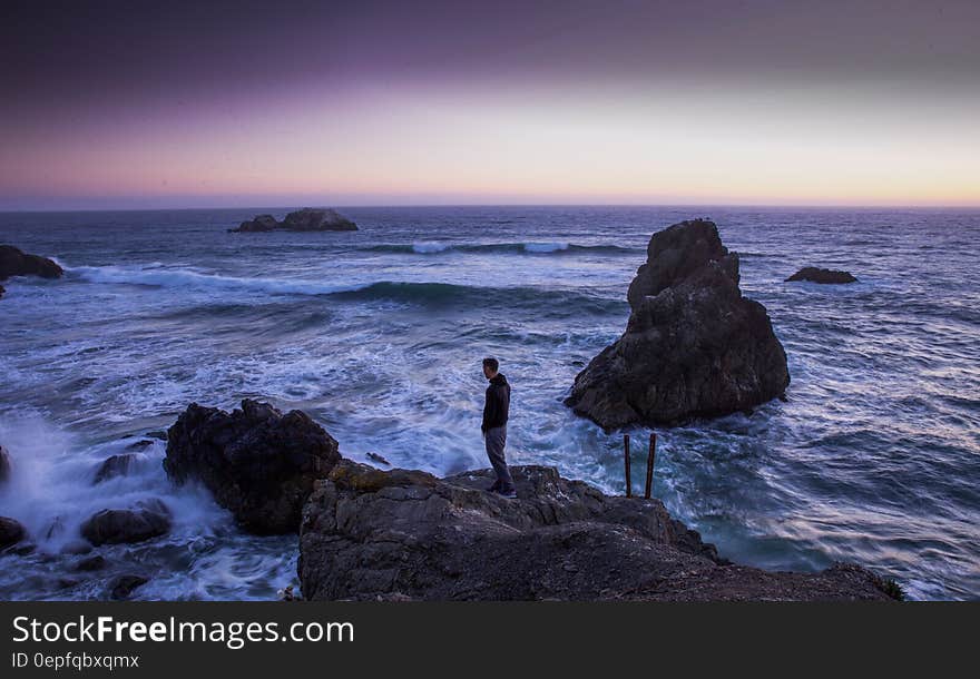 Man in Black Shirt Standing on Rock in Between Sea Water