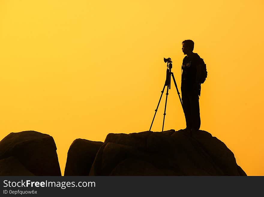 Silhouette of photographer of rocky crag against yellow skies at sunset.