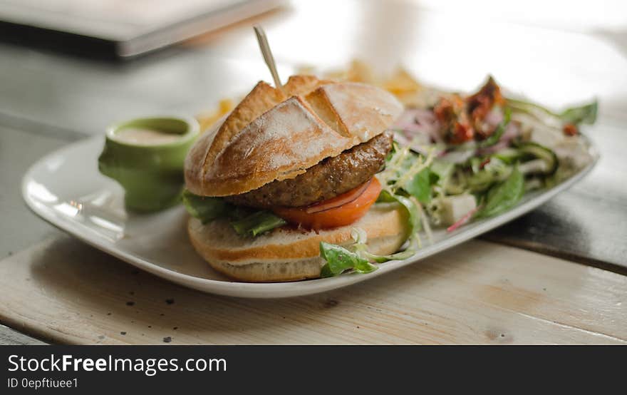 Hamburger on bun with salad on white china plate on tabletop. Hamburger on bun with salad on white china plate on tabletop.