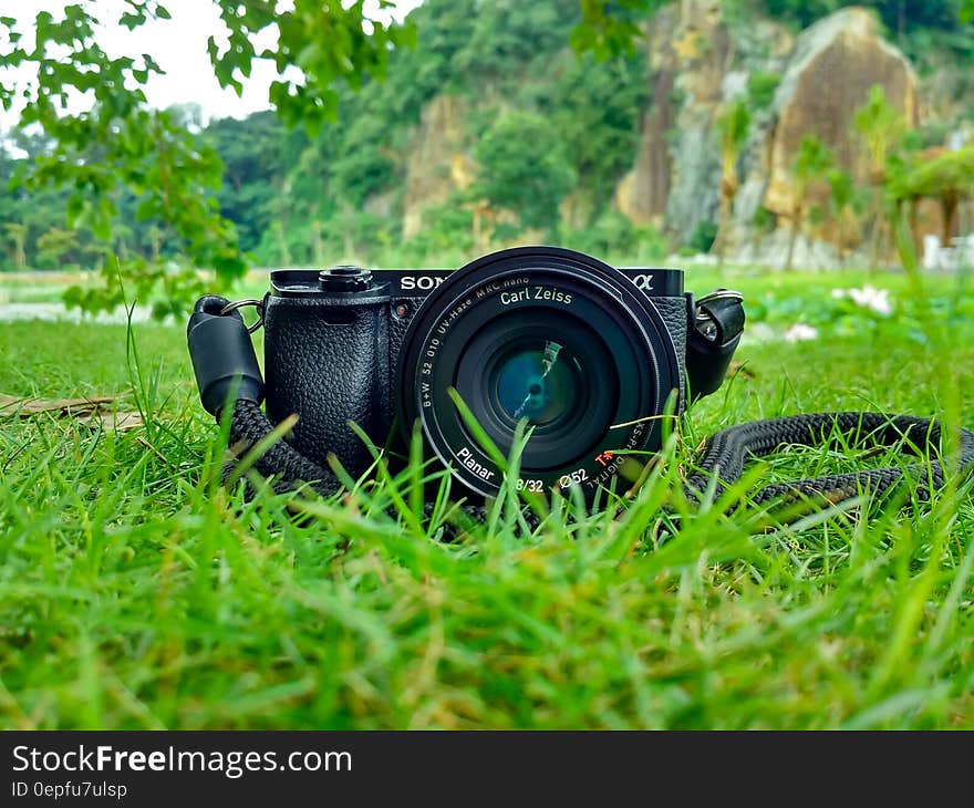 Black Sony Dslr Camera on Green Grass in Front of Brown and Green Mountain