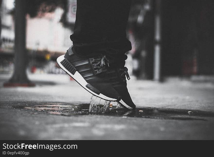 Grayscale Photo of Person Wearing Adidas Nmd Jumping on Puddle