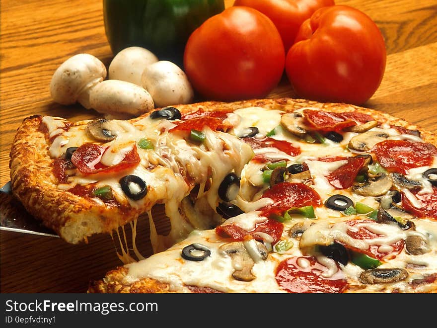 Close up of pizza pie with fresh tomatoes and mushrooms on wooden table. Close up of pizza pie with fresh tomatoes and mushrooms on wooden table.