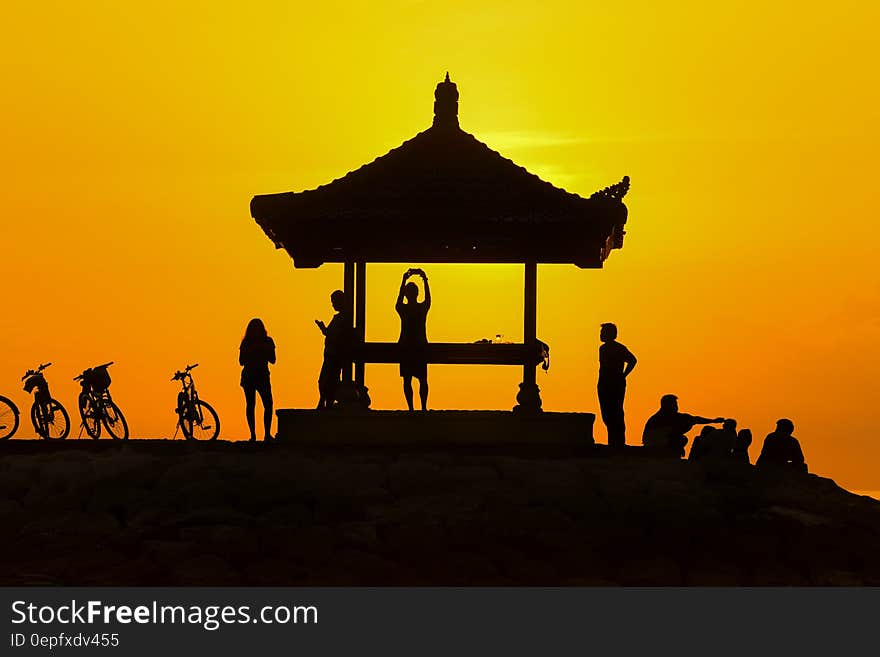 Young people in silhouette on a hilltop with light from a golden sunset and with an Asian style shelter and bicycles propped up nearby. Young people in silhouette on a hilltop with light from a golden sunset and with an Asian style shelter and bicycles propped up nearby.