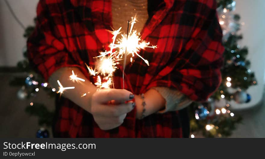 Hand holding sparkler indoors with Christmas tree in background.