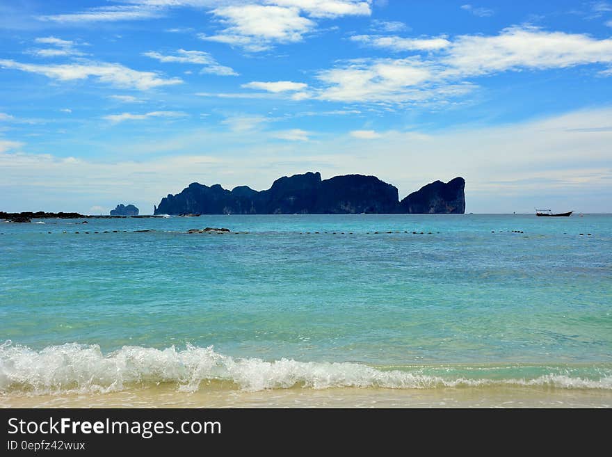 View of sandy beach by the blue sea with rocky islands off the coast.