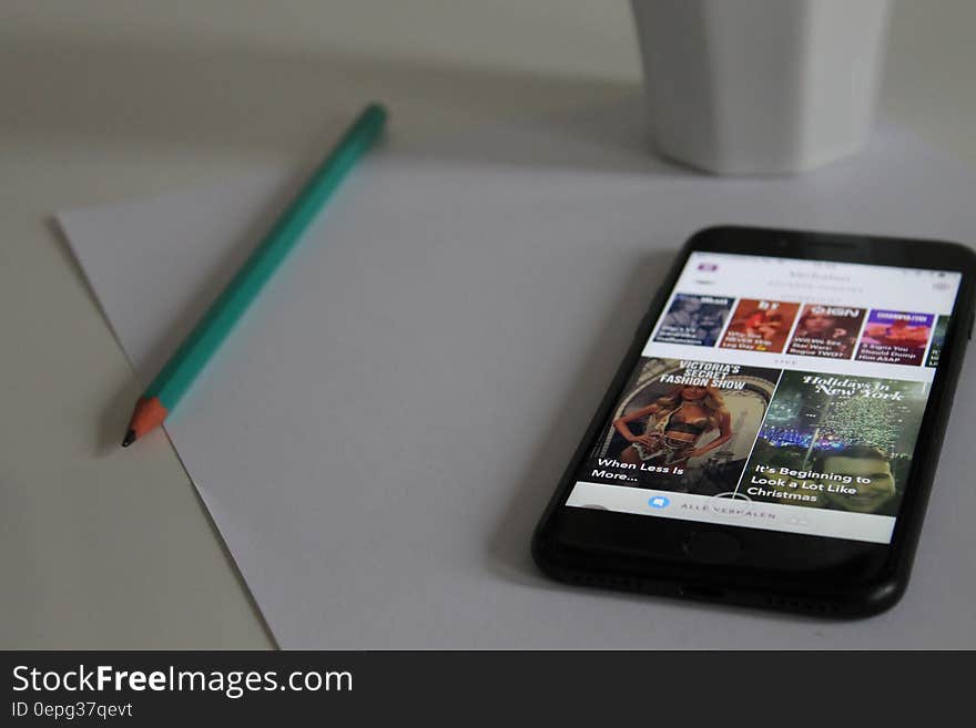 A smartphone on a piece of paper with pencil and a cup. A smartphone on a piece of paper with pencil and a cup.