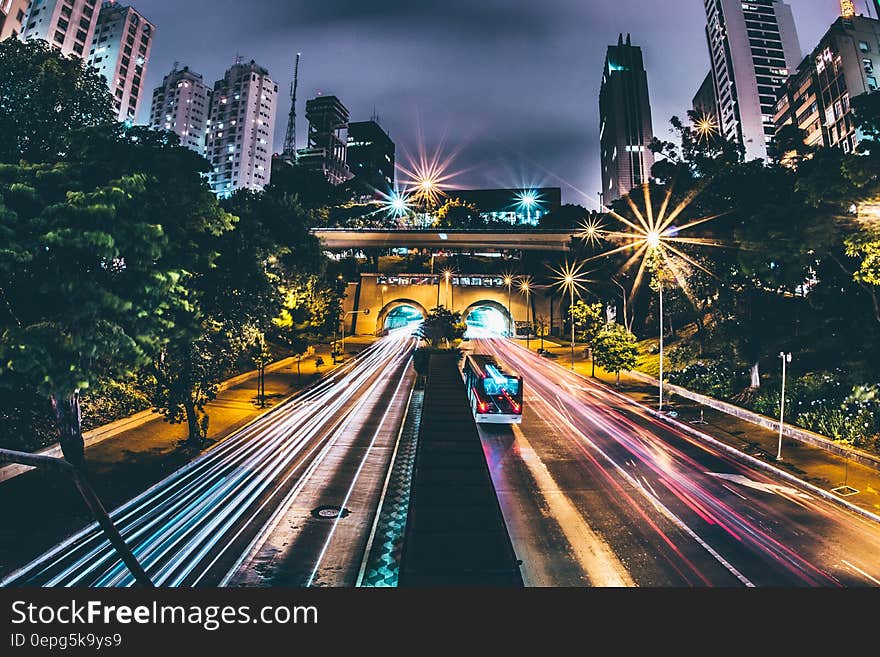 Highway with red and white traffic trails, caused by vehicles going towards and leaving a city at dusk with Skyscrapers and road or railway bridge above the main highway. Highway with red and white traffic trails, caused by vehicles going towards and leaving a city at dusk with Skyscrapers and road or railway bridge above the main highway.