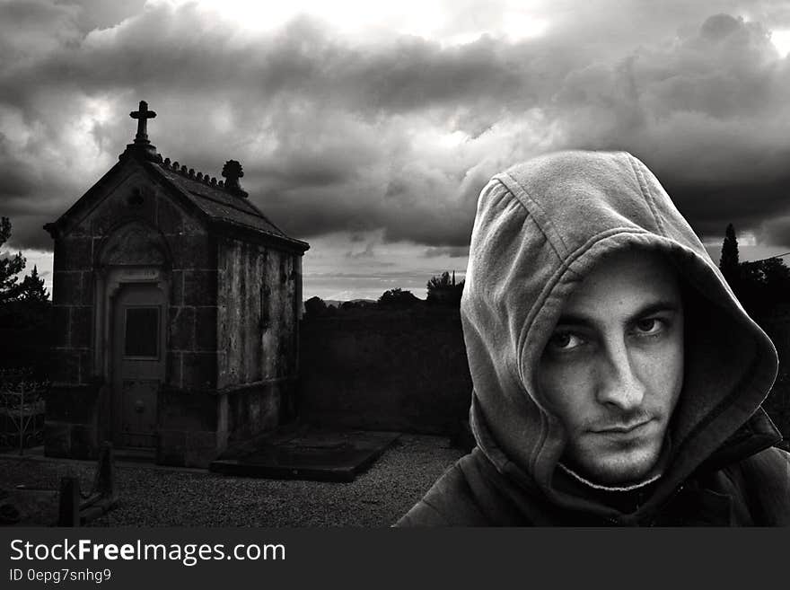 Man in hoodie jacket standing next to vault in cemetery in black and white. Man in hoodie jacket standing next to vault in cemetery in black and white.