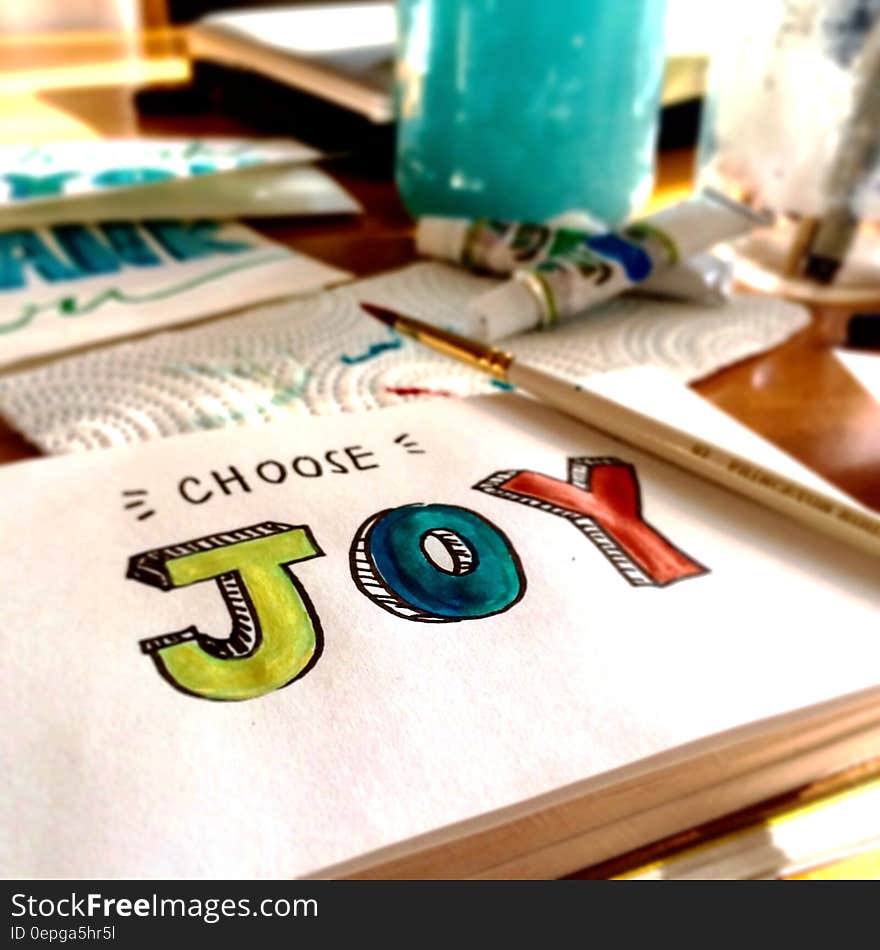 Choose joy illustrated on white paper with paintbrush and paints on tabletop.