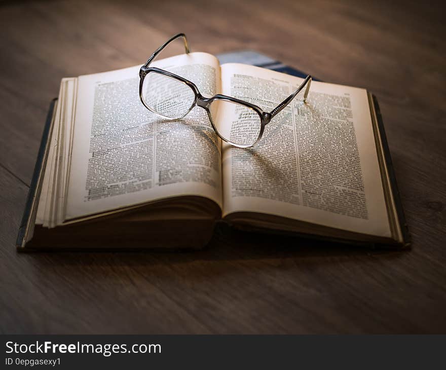 Eyeglasses on top of open book on wooden desk. Eyeglasses on top of open book on wooden desk.