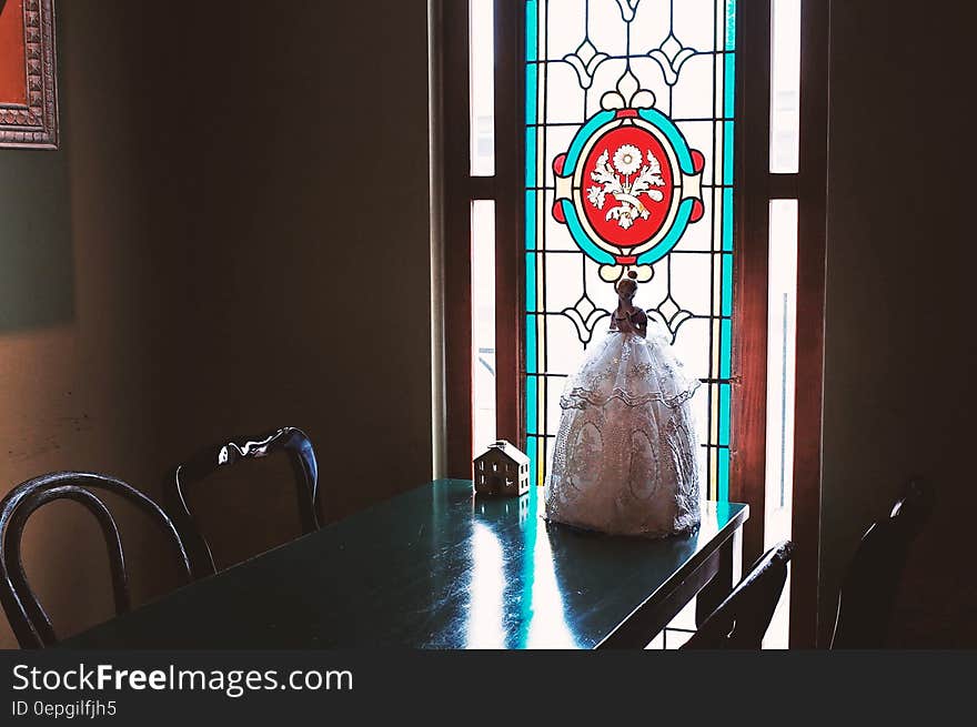 Dolls on wooden table inside room with stained glass panel in window. Dolls on wooden table inside room with stained glass panel in window.