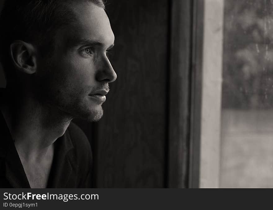 Black and white side portrait of thoughtful young man looking out of window.