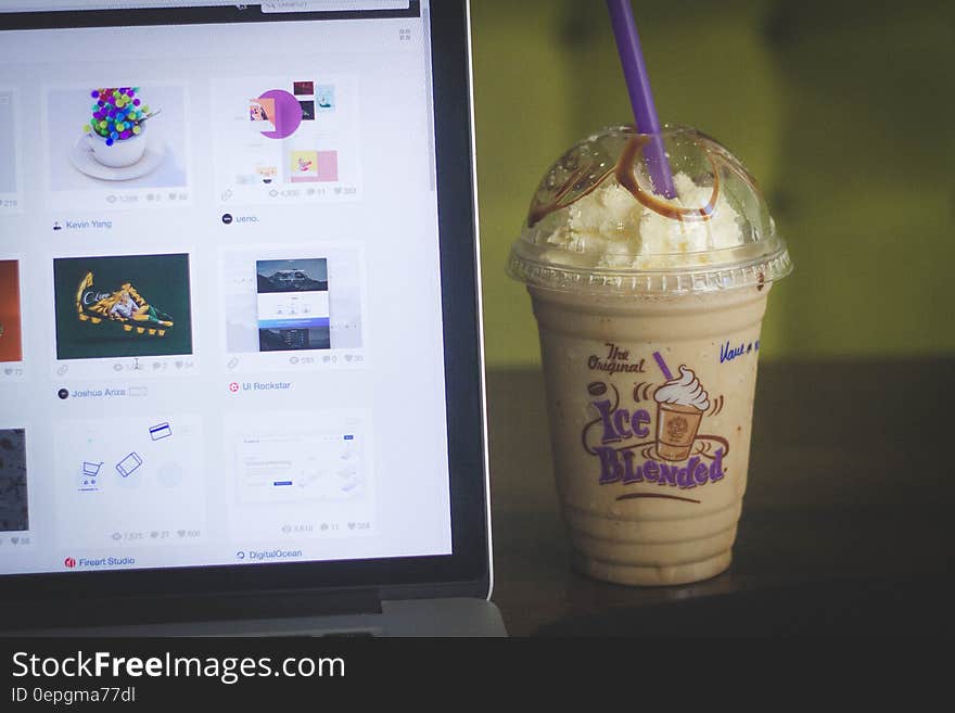 Iced coffee drink in plastic cup next to laptop computer screen. Iced coffee drink in plastic cup next to laptop computer screen.