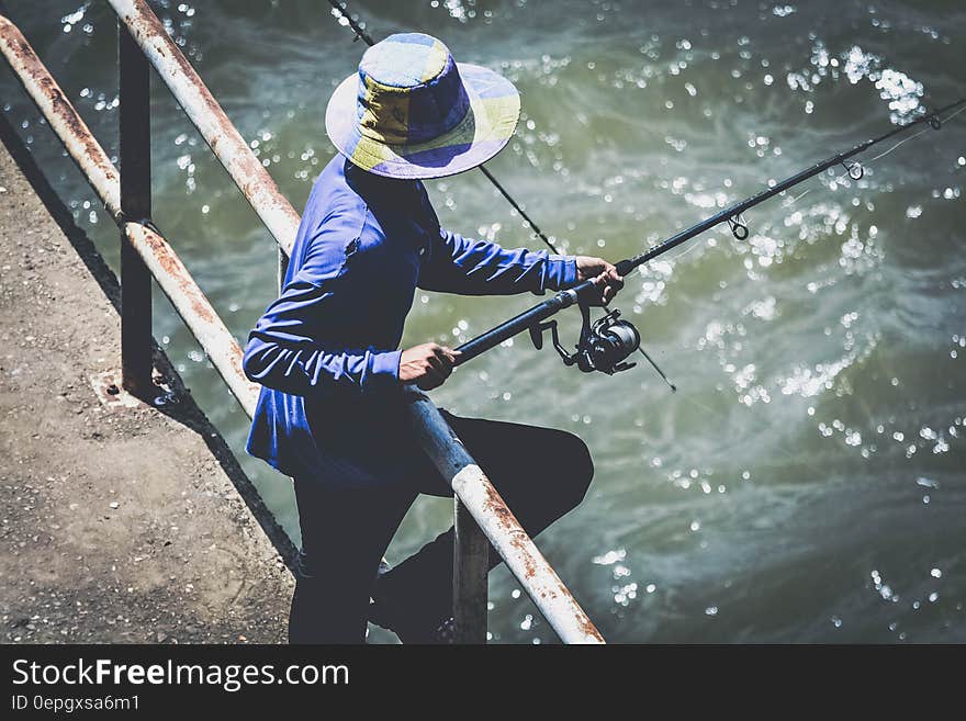 Person in Blue Long Sleeve Shirt and Black Pants Using Fishing Rod