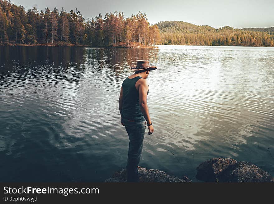 Man standing on banks of tree lines lake on sunny day. Man standing on banks of tree lines lake on sunny day.