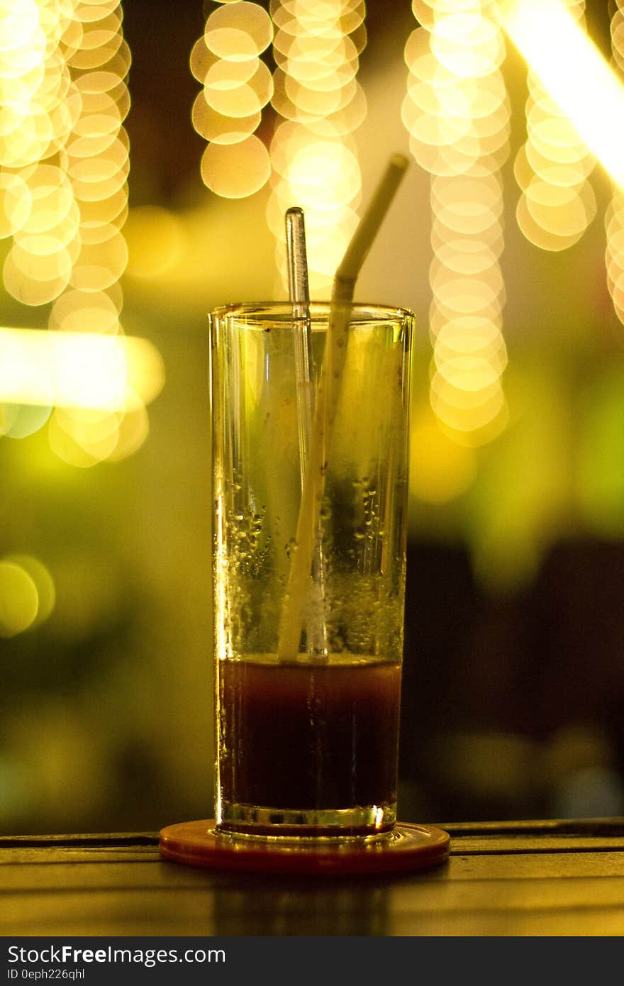 Glass with red beverage and straw on coaster on bar with bokeh lights. Glass with red beverage and straw on coaster on bar with bokeh lights.