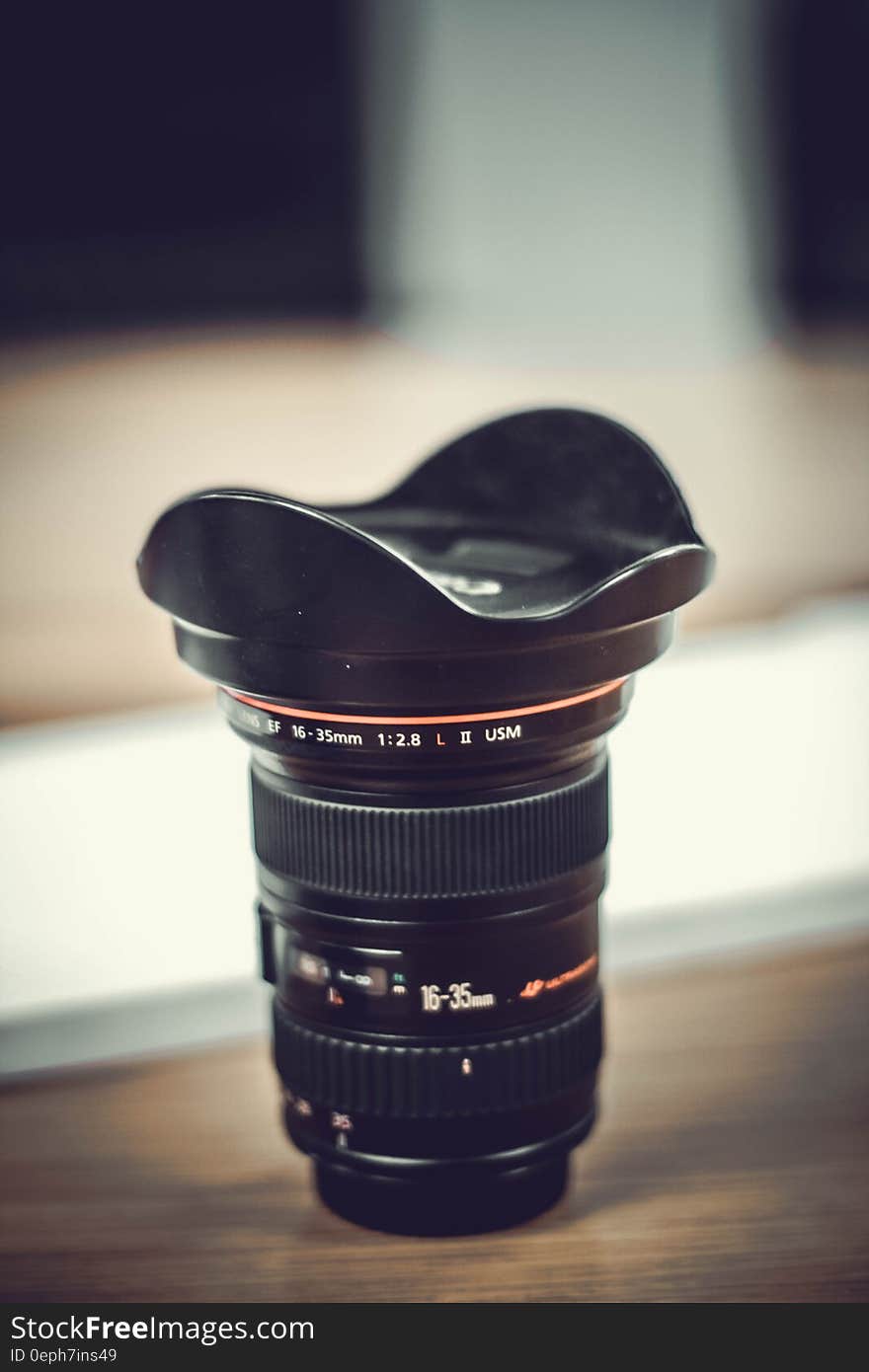 Close up of Canon lens with hood on wooden table. Close up of Canon lens with hood on wooden table.