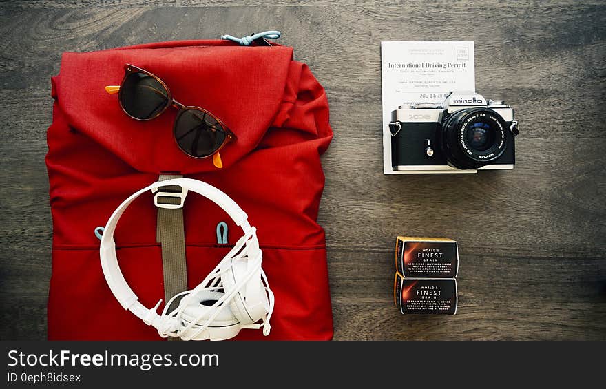 Travel still life of red backpack with sunglasses, headphones, camera and film on wooden boards. Travel still life of red backpack with sunglasses, headphones, camera and film on wooden boards.