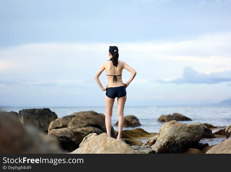 A young woman in bikini standing on a sea rock. A young woman in bikini standing on a sea rock.