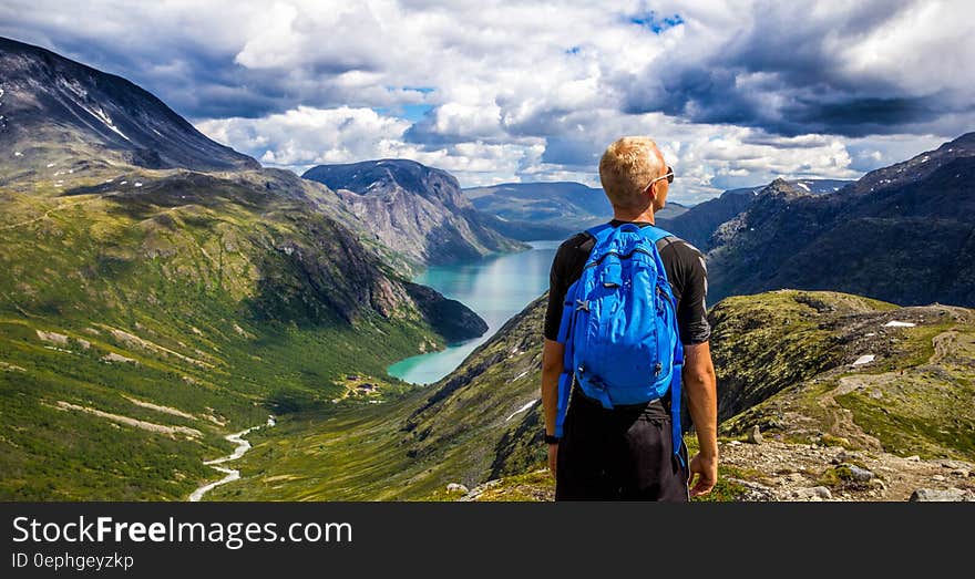 A hiker with a backpack on a mountain peak in Norway and a view of the slopes and a lake in the distance. A hiker with a backpack on a mountain peak in Norway and a view of the slopes and a lake in the distance.