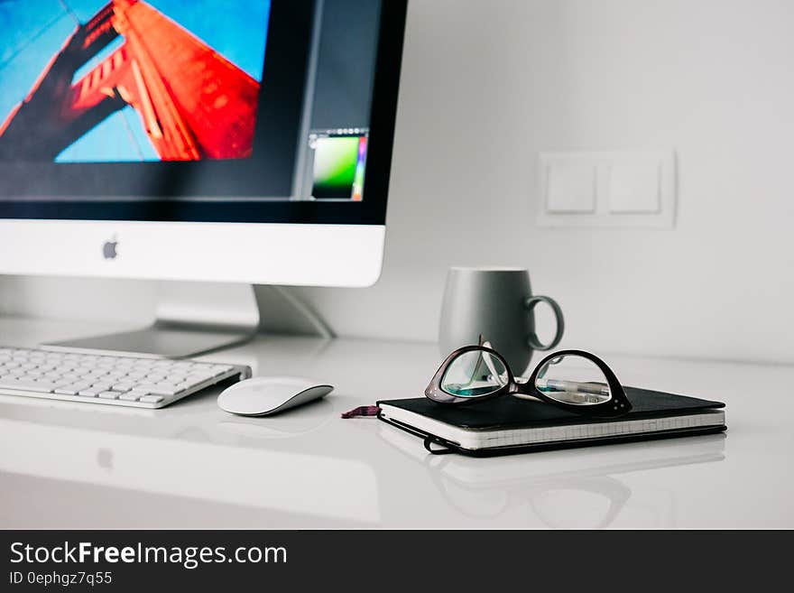 Silver Imac Turned on Beside Gray Ceramic Mug and Black Frame Eyeglasses