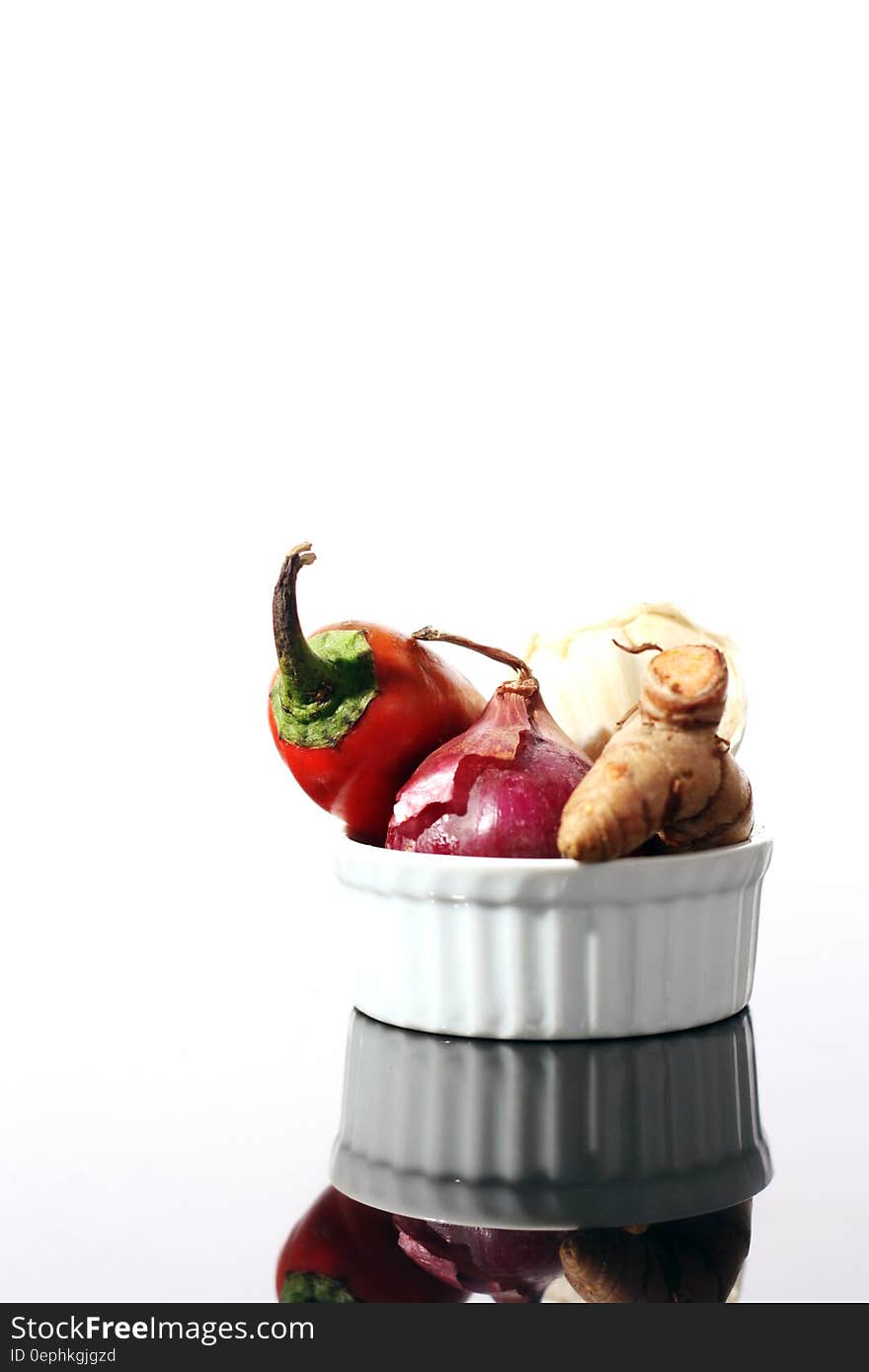 White bowl with red chili pepper, ginger root and onion on counter. White bowl with red chili pepper, ginger root and onion on counter.