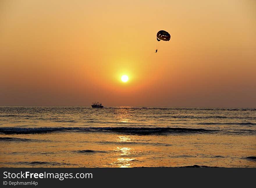 Parasailing behind boat on water at sunset. Parasailing behind boat on water at sunset.