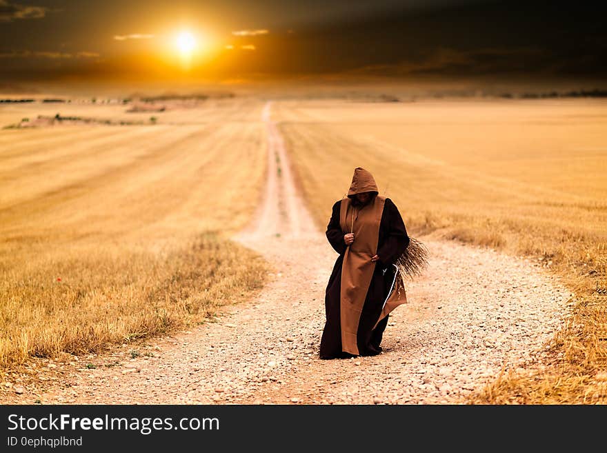 Person in Brown and Black Robe in the Middle of the Road