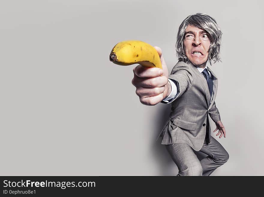 Man in Gray Suit Jacket Holding Yellow Banana Fruit While Making Face