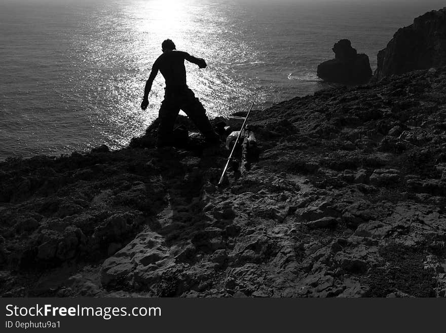 Silhouette of fisherman on rocky shores at sunrise in black and white. Silhouette of fisherman on rocky shores at sunrise in black and white.