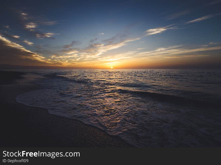 Panoramic view of waves breaking on beach at sunset.