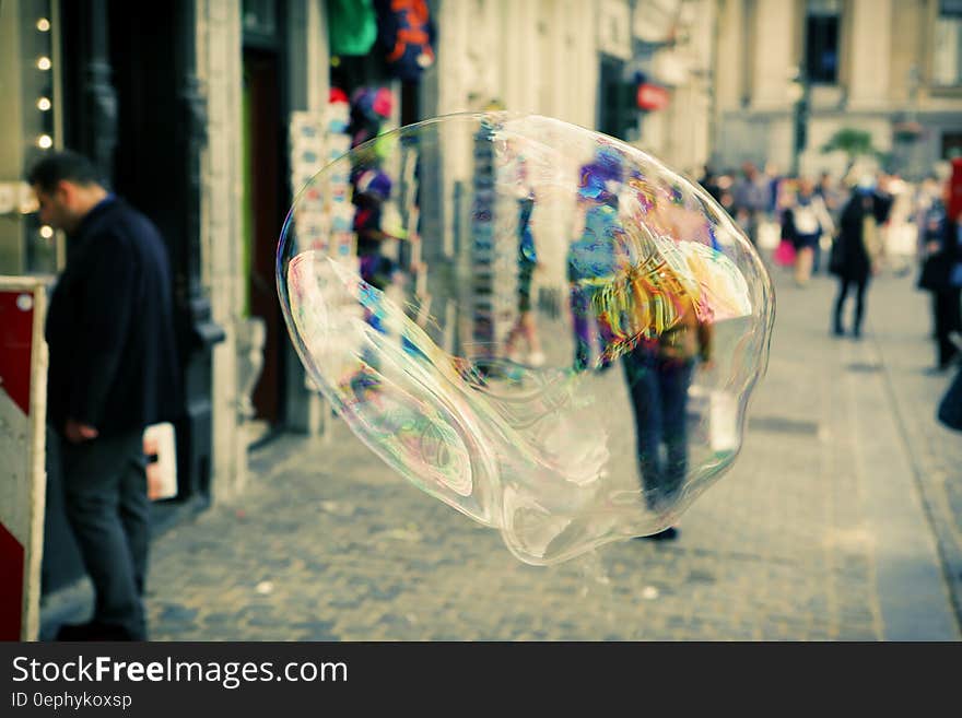 Closeup of very large soap bubble floating in the city street just above the pavement blurring an approaching shopper carrying a carrier bag. Closeup of very large soap bubble floating in the city street just above the pavement blurring an approaching shopper carrying a carrier bag.