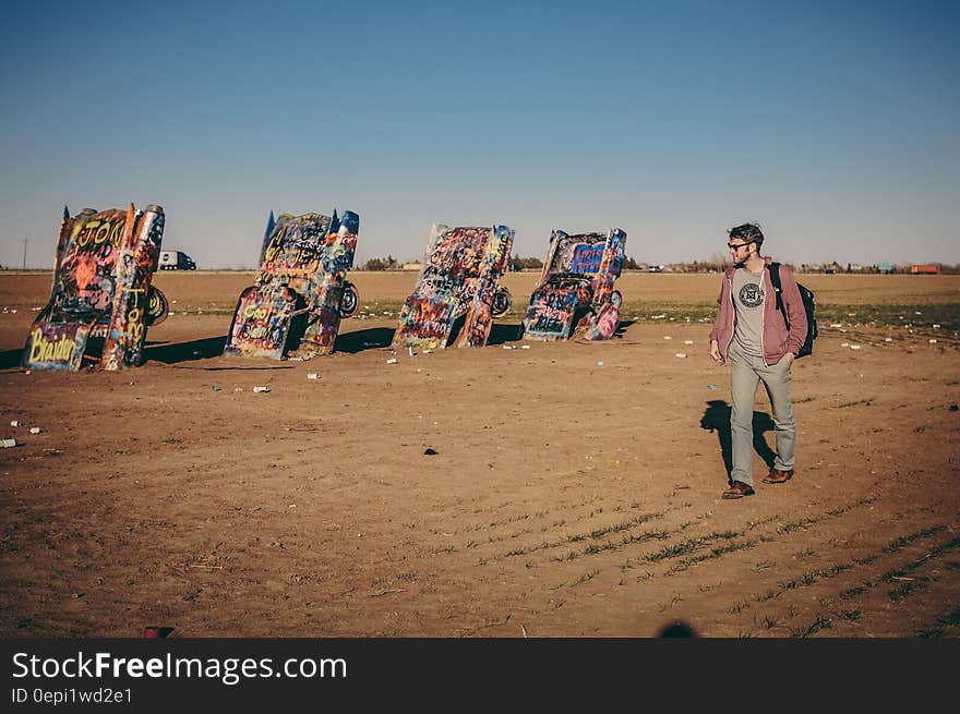 Art installation known as the Cadillac ranch with half-buried cars and a man walking past them.
