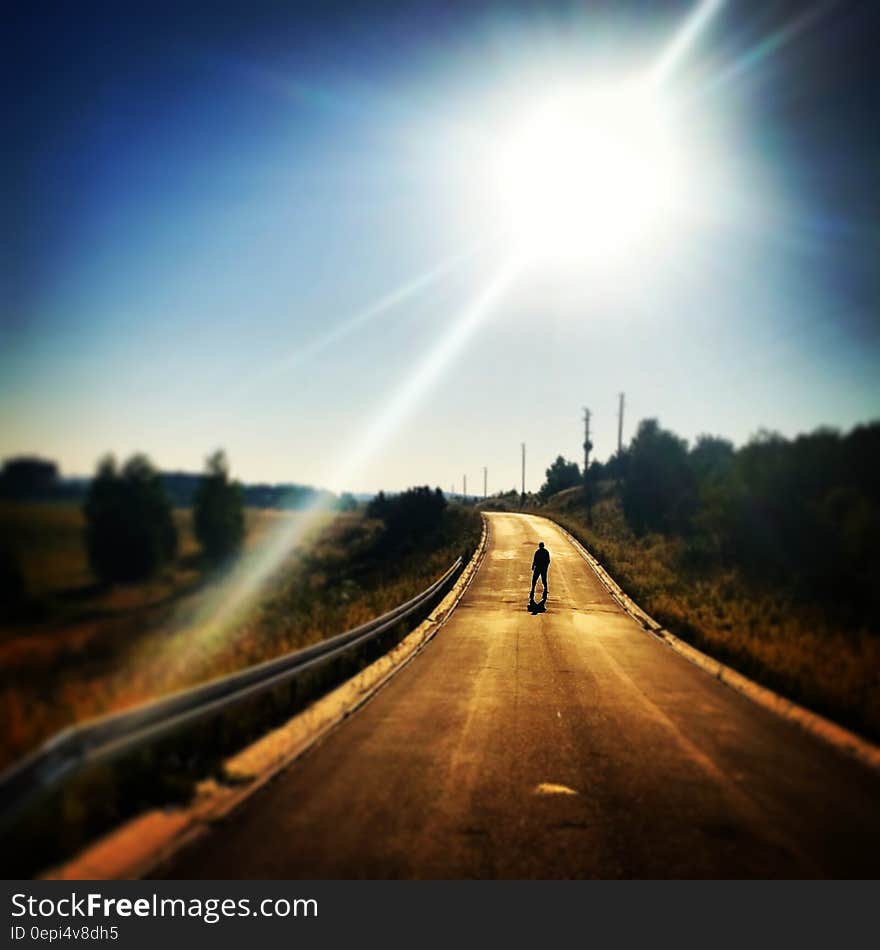 Person Standing on Blacktop Road Under Blue Sky During Daytime