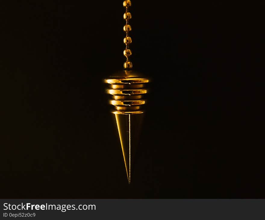 A close up of a gold pendulum on a black background.