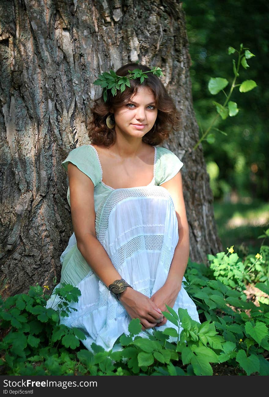 Smiling Woman Wearing Green Leaf Crown With Green and White Sleeveless Dress Sitting in Green Leaf during Day Time