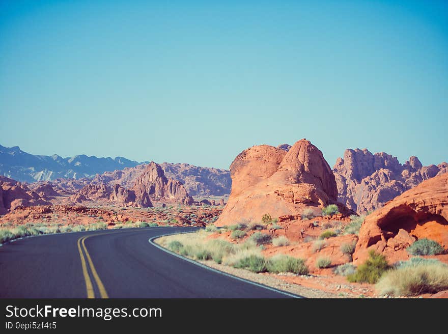 Sharp corner of road with central yellow marking leading through red rocky desert countryside, pale blue sky background. . Sharp corner of road with central yellow marking leading through red rocky desert countryside, pale blue sky background. .