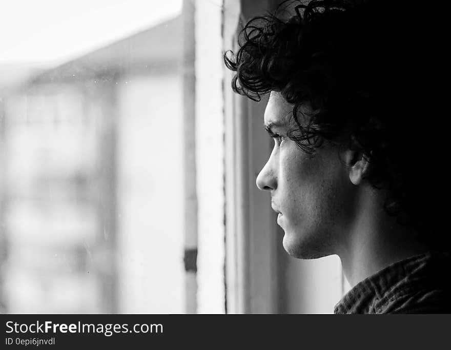 A young man looking pensively through a window. A young man looking pensively through a window.