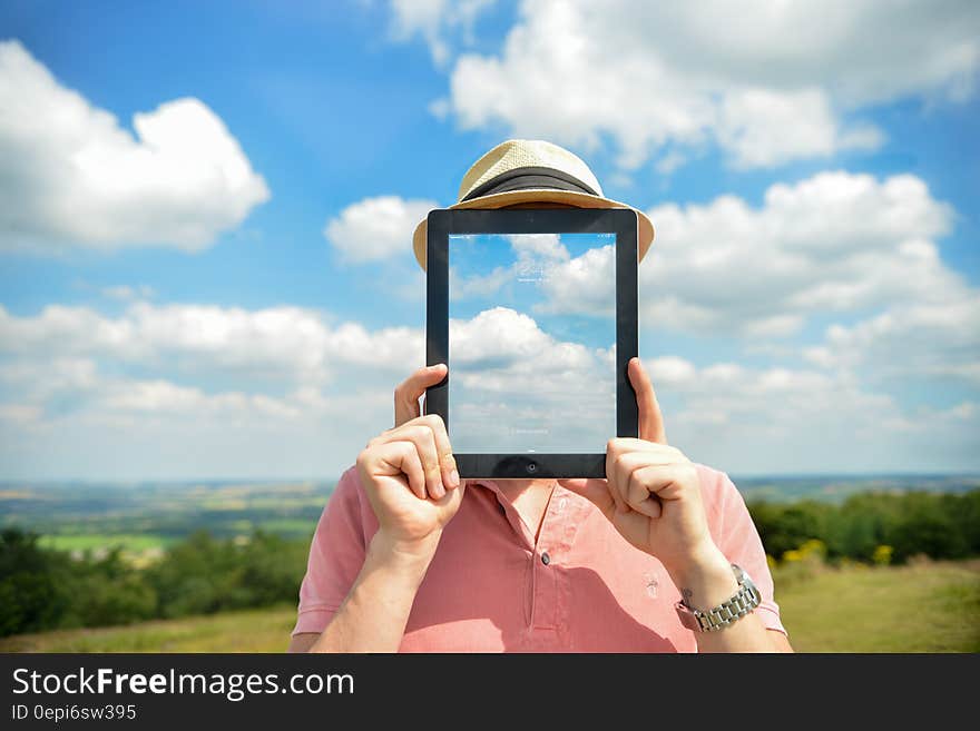 A portrait of a man outdoor holding an iPad in front of his face, with a sky wallpaper over his face. A portrait of a man outdoor holding an iPad in front of his face, with a sky wallpaper over his face.