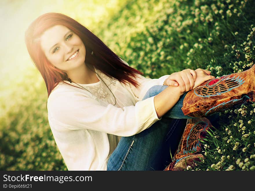 Woman in White Long Sleeve Shirt Sitting on Grass Field during Daytime