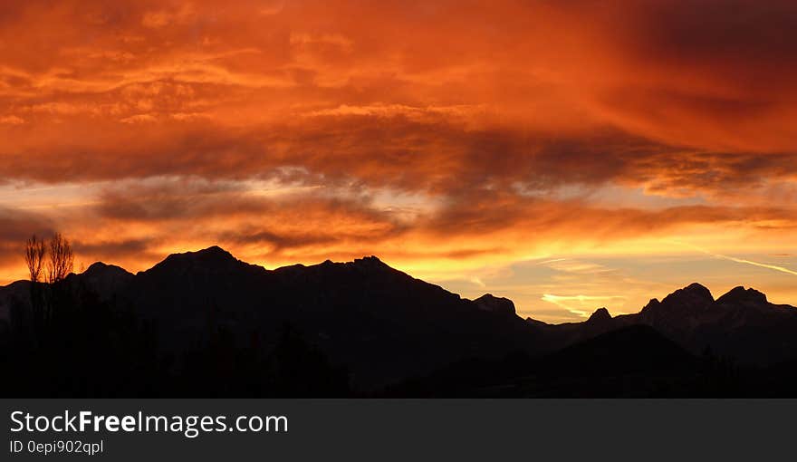 Mountain range in silhouette with dramatic orange and yellow sky at sunrise. Mountain range in silhouette with dramatic orange and yellow sky at sunrise.