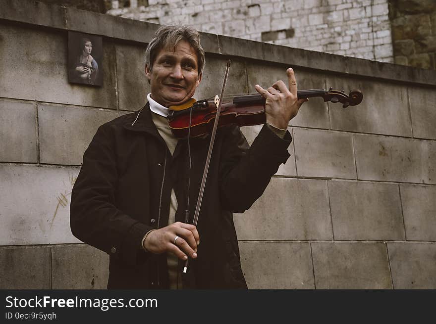 Smiling Standing Man Playing Violin by Gray Stone Wall