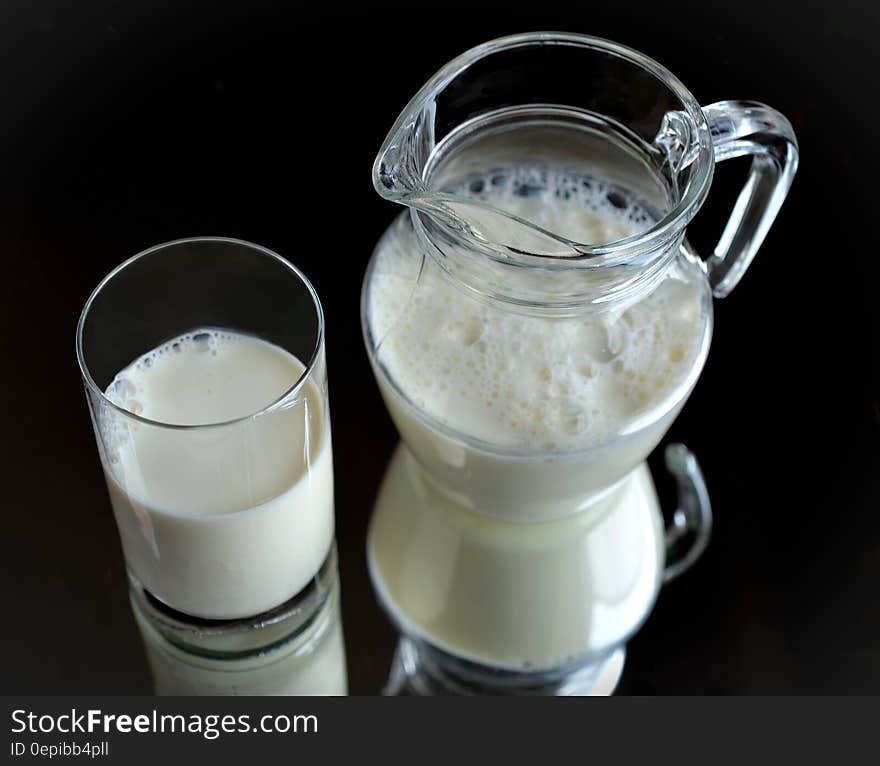 Jug of milk and glass of milk side by side on a black reflective surface. Jug of milk and glass of milk side by side on a black reflective surface