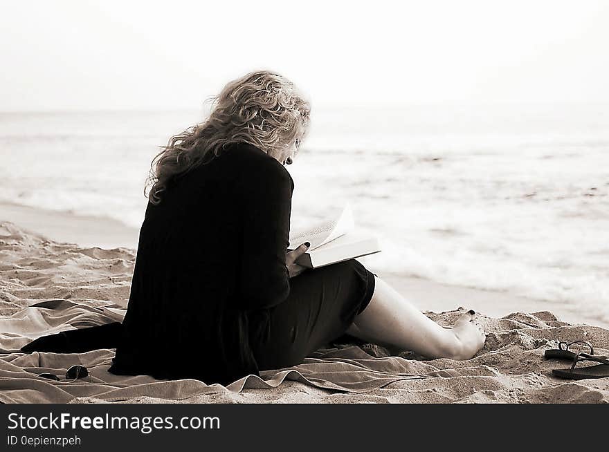 Person Sitting on the Seashore While Reading a Book