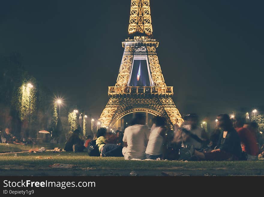 People gathered sitting on the grass by the illuminated Eiffel tower at night. People gathered sitting on the grass by the illuminated Eiffel tower at night.