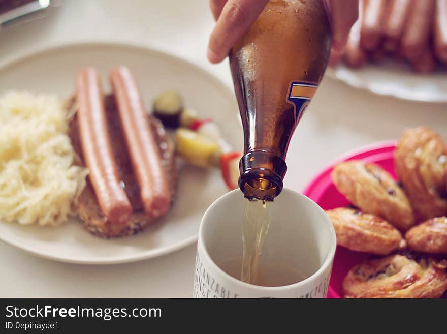 Close up of beer pouring from bottle to glass on table with German sausages and sauerkraut. Close up of beer pouring from bottle to glass on table with German sausages and sauerkraut.